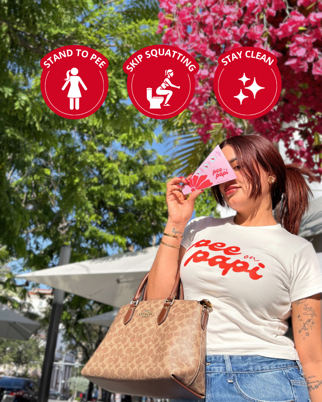 A woman outdoors wearing a white graphic T-shirt with red text that reads 'pee on papi' and holding a pink product package. Red circular callout graphics above show icons and the words 'STAND TO PEE', 'SKIP SQUATTING', and 'STAY CLEAN'.